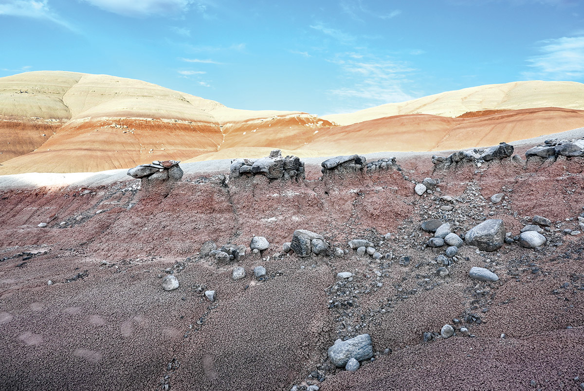 The Brushy Basin Member and close-up view of “popcorn” weathering. Shoe prints for scale. Layered ochre and beige desert hills under a blue sky with rocky foreground.
