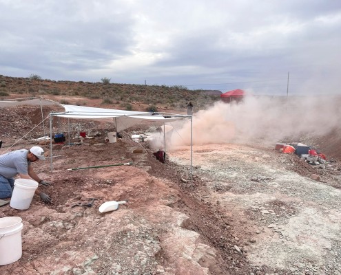 A canopy above rock surface and dust blowing where the dig site is located.