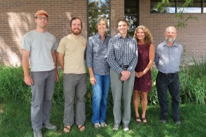 Six people posing for a photo in front of a brick building.