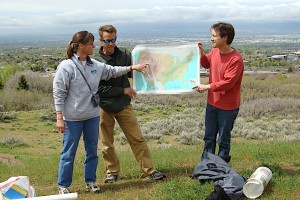 Two people holding a map of the United States. One person pointing at the western half.