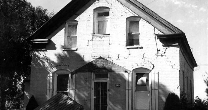 Black and white photo of a brick house with many cracks.