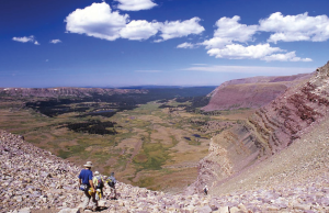 Three hikers going downhill among loose rock and horizontal layers of rock.
