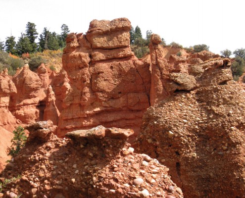 Red rock wall and hoodoos with a conglomerate rock layer in the foreground.