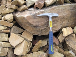 A close-up of quartzite ashlar blocks and a boulder; rock hammer for scale at West Mountain Community Pit.